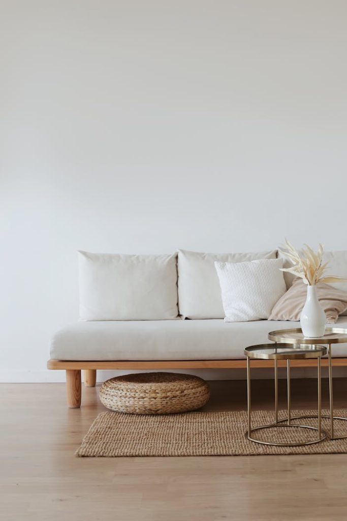 white-couch-on-wooden-floor-4352247 A chic minimalist living room featuring a white sofa with cushions, dried flowers in a vase, and a wooden floor.
